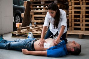 Symbolbild: Frau klebt reglosem Mann am Boden Defibrillator Elektroden-Pflaster an