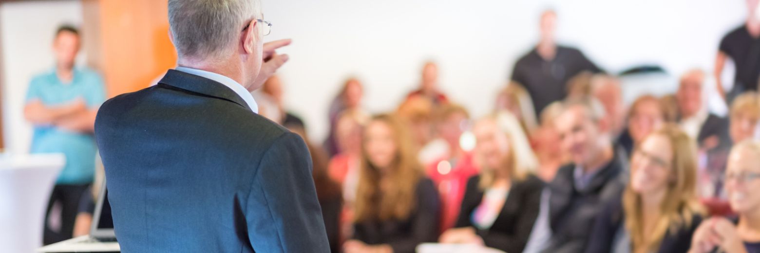 Bannerbild, Wolfgang de Haan steht lehrend vor einer Gruppe Menschen