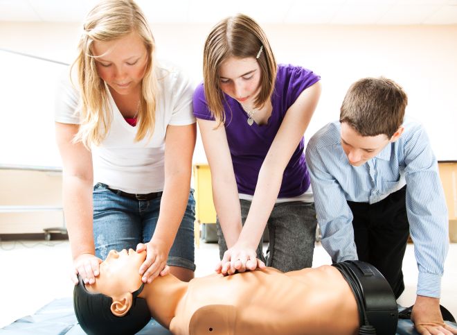 Symbolbild: drei Kinder lernen an einer Puppe Herzdruckmassage